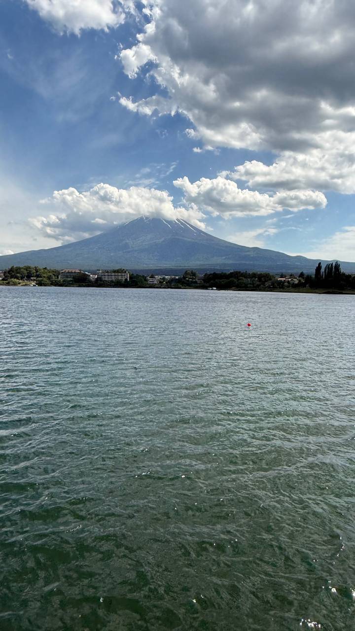 Snow-capped Mount Fuji towers over a calm lake with a town lining the far shore.