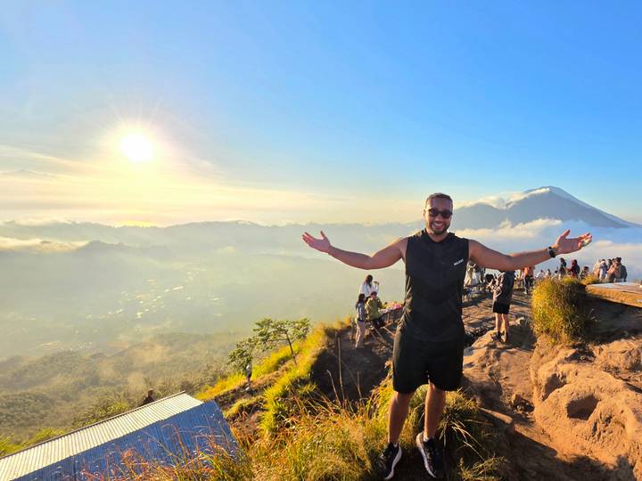 Hiker raises arms in triumph atop Mount Batur at sunrise with sea of clouds and volcano backdrop