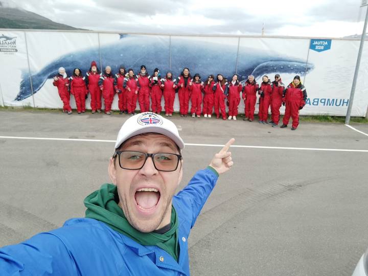 Excited man in foreground points at a line of people in red flotation suits before a whale mural