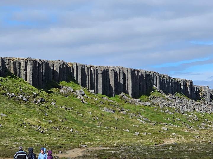 Dramatic wall of gray columnar basalt rising above green grass and scattered rocks