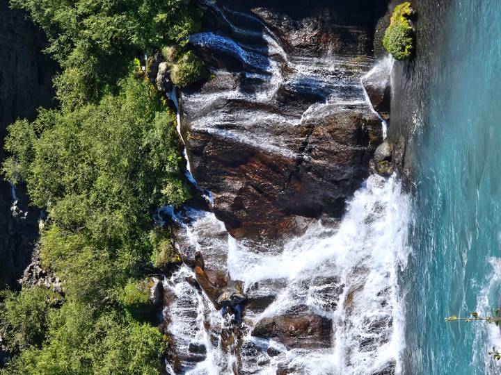 Clear turquoise water cascades over multi-tiered lava rock waterfall surrounded by greenery