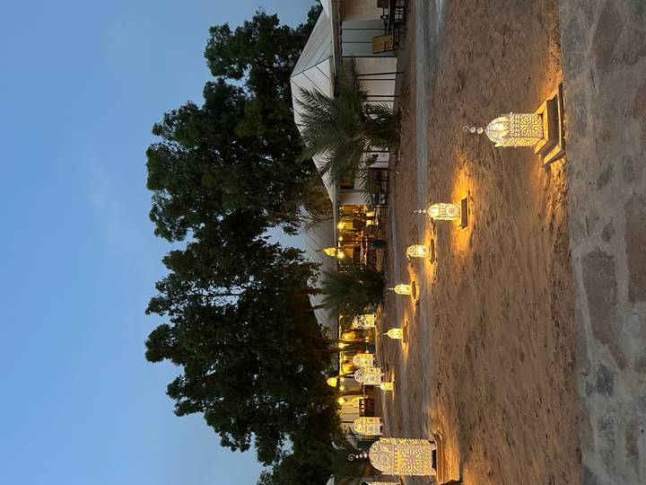 Desert camp pathway lined with illuminated Moroccan lanterns leading to canvas tents at dusk