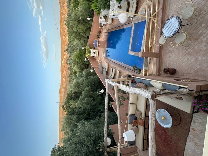 Elegant riad rooftop with blue pool, cushioned lounges and olive trees overlooking desert town