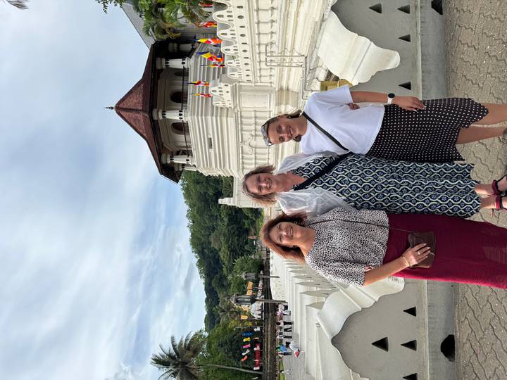 Three women posing in front of the Temple of the Tooth’s white stupa and moat in Kandy