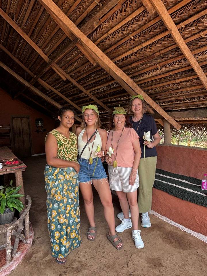 Small group wearing lotus leaf hats and holding flowers inside a rustic Sri Lankan homestead