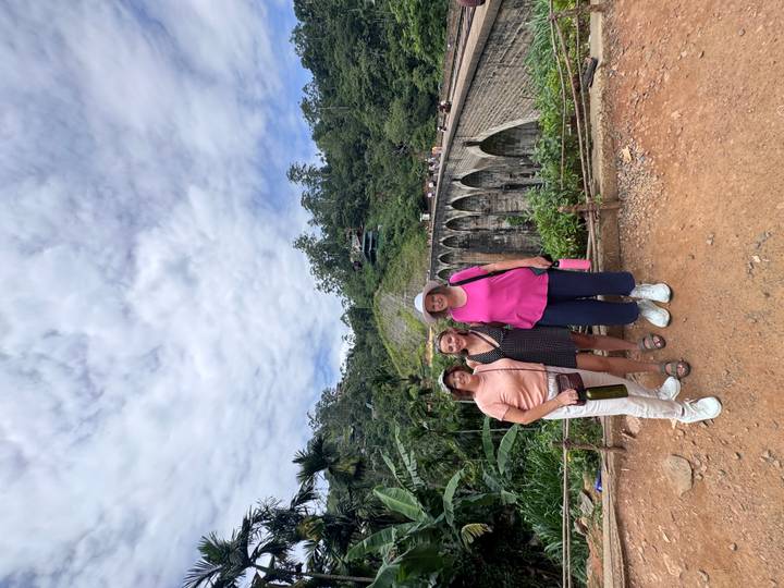 Three women pose in front of Sri Lanka’s Nine Arches Bridge with jungle scenery and cloudy sky