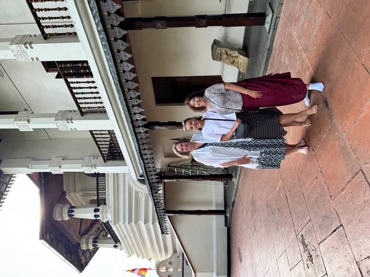 Three women dressed modestly stand barefoot outside the ornate white Temple of the Tooth in Kandy