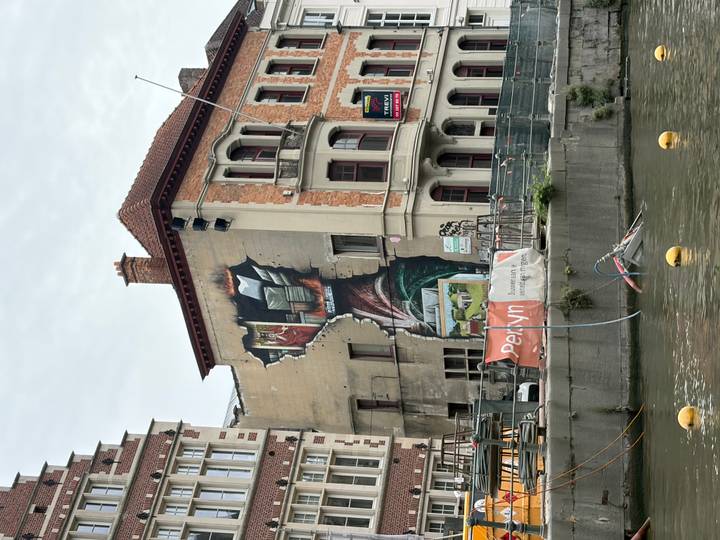 Colorful street art mural covers a partially demolished riverside building in Ghent with construction nearby