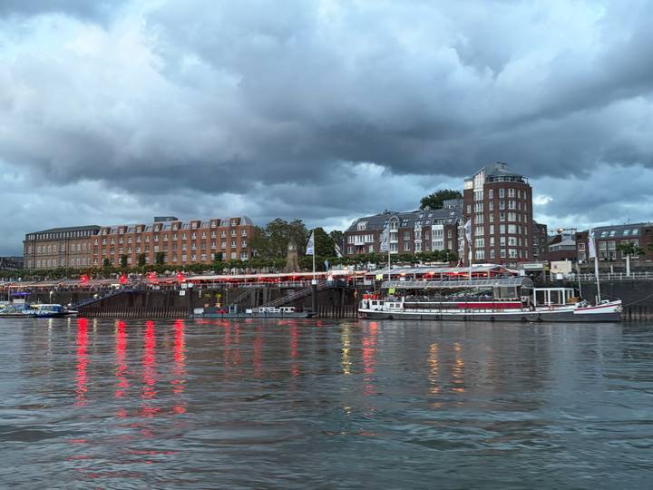 Riverside cityscape at dusk with restaurant lights reflecting red on the water beside moored boats