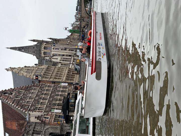 Sightseeing boat full of visitors glides through Ghent’s canal with historic guild houses behind