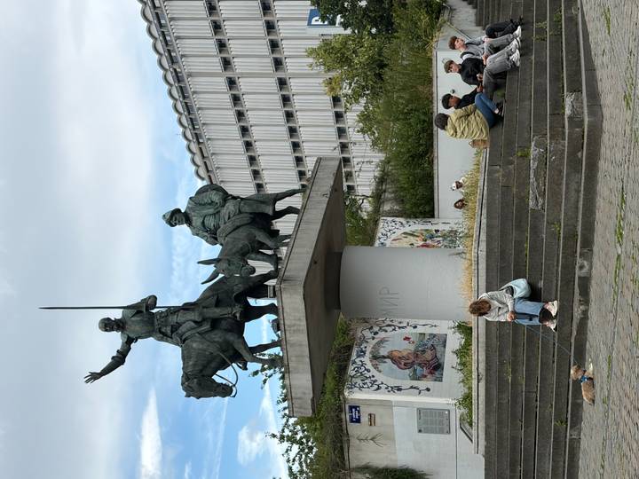 Bronze statue of Don Quixote and Sancho Panza on horseback in a public square with people sitting nearby