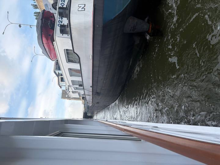 A dark cargo barge passes closely beside a white passenger vessel within a narrow waterway lock.