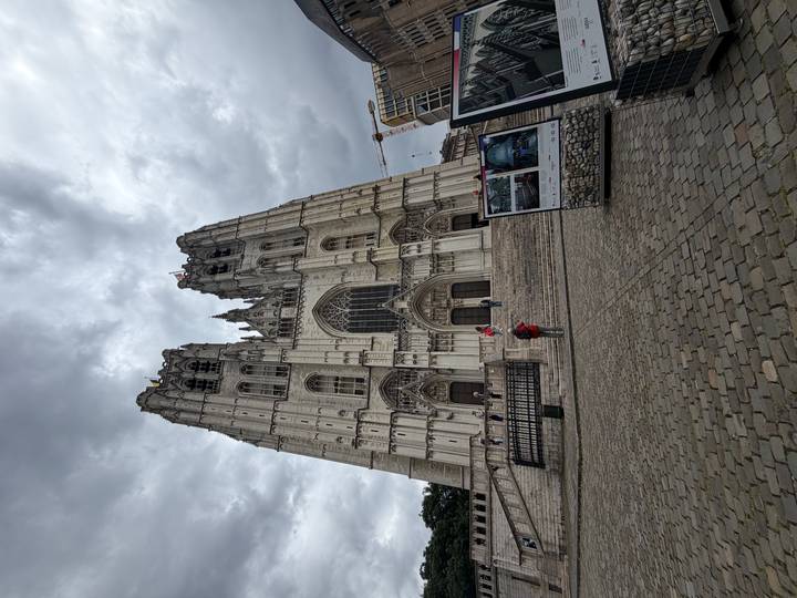 Imposing Gothic façade of St. Michael and St. Gudula Cathedral rising into a dramatic cloudy sky, visitors standing on the broad steps.