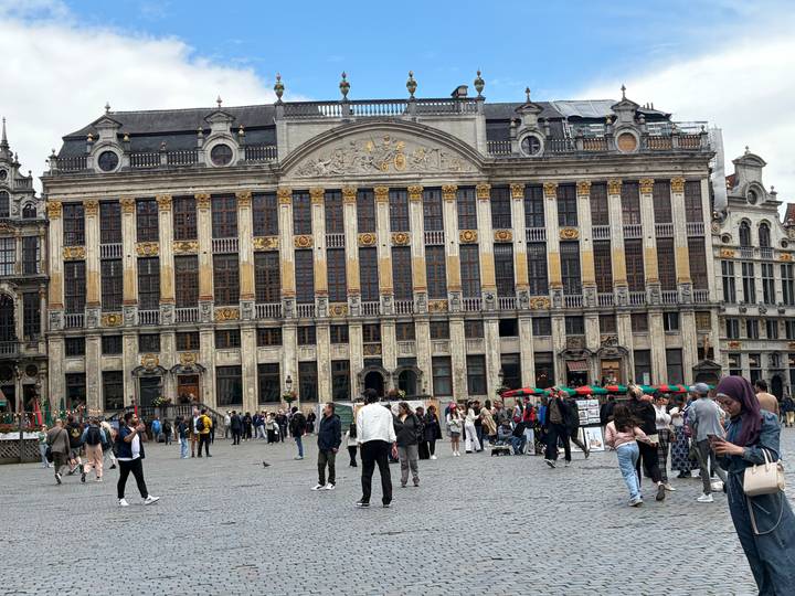 Broad view of the ornate guildhall on Brussels’ Grand Place with crowds of tourists and locals in the square.