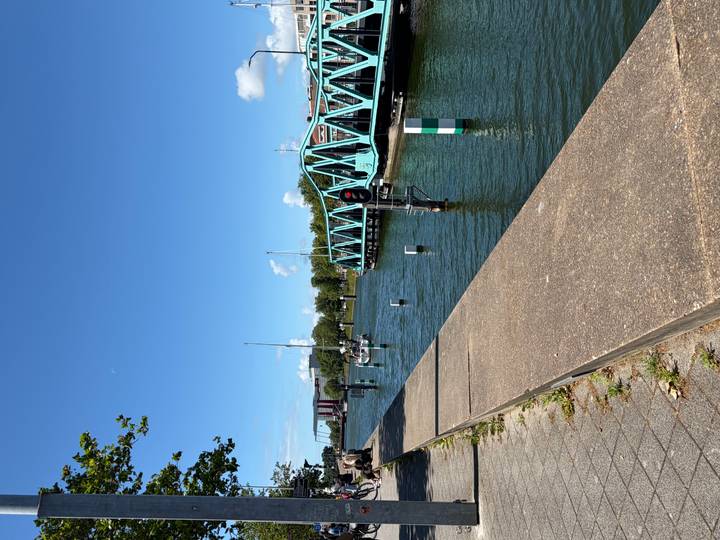 Calm canal bordered by a turquoise lifting bridge and moored sailboats on a bright summer day.