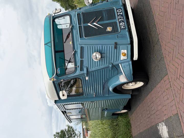 Retro blue Citroën food truck parked on a brick roadside with cloudy skies overhead.