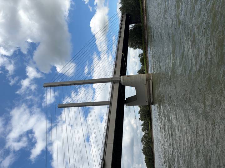 Modern cable-stayed bridge spanning a wide river with scattered clouds in a blue sky.