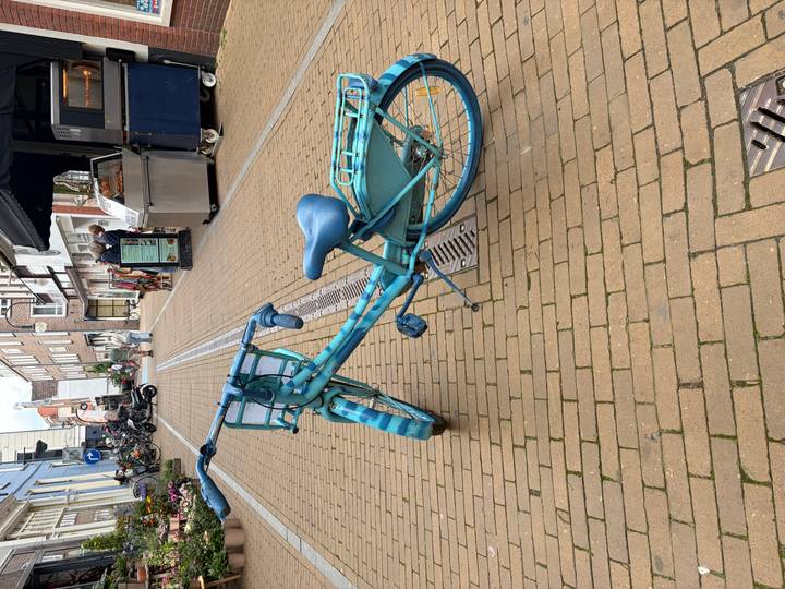Bright turquoise bicycle lying on its side on a brick pedestrian street in a small town.