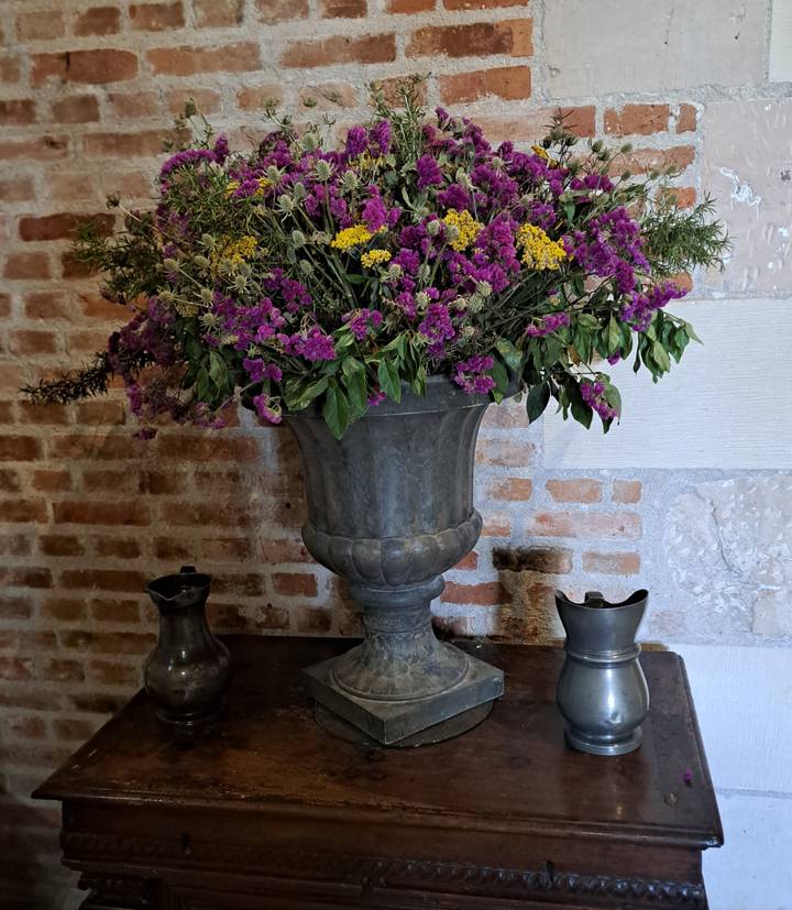 Large pewter urn filled with purple and yellow flowers against an old brick wall