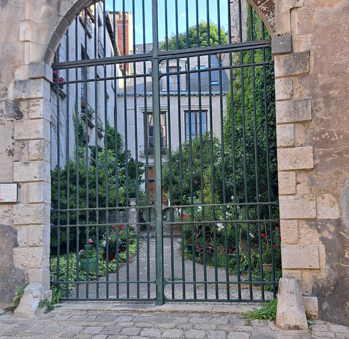 Tall iron gate revealing a lush hidden courtyard and stone townhouse façade