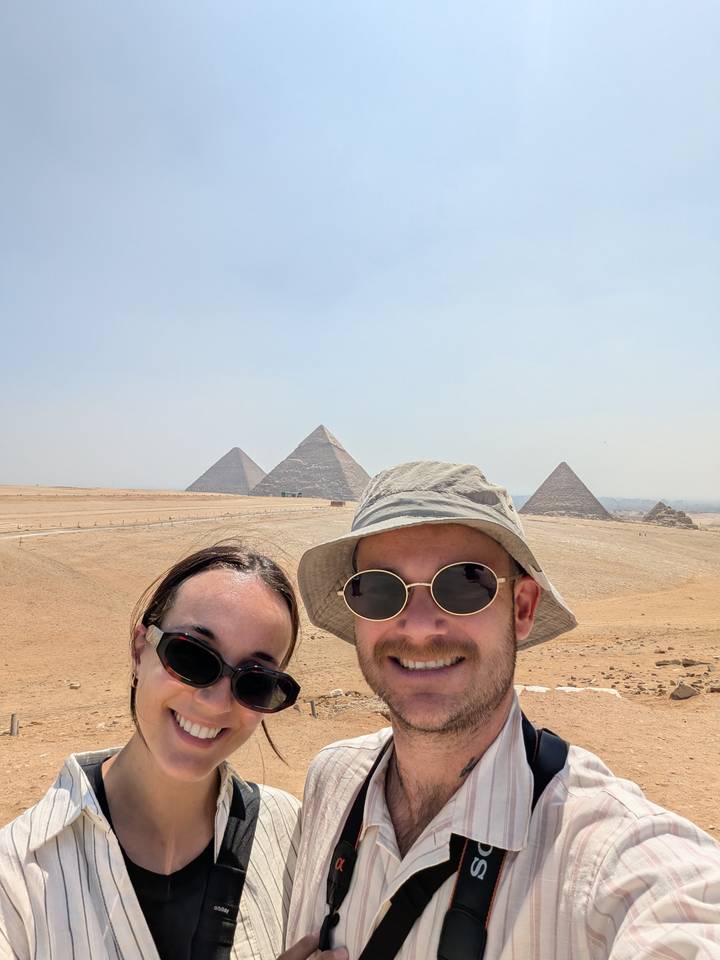 Couple selfie with the pyramids rising from the desert plateau behind them