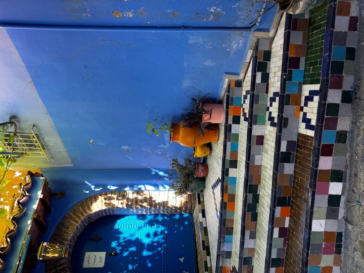 Colorful tiled staircase beside vivid blue walls and pottery in a Moroccan alley.