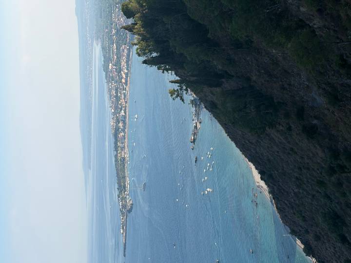 High coastal view of blue bay dotted with boats and a distant city on the Sicilian shore