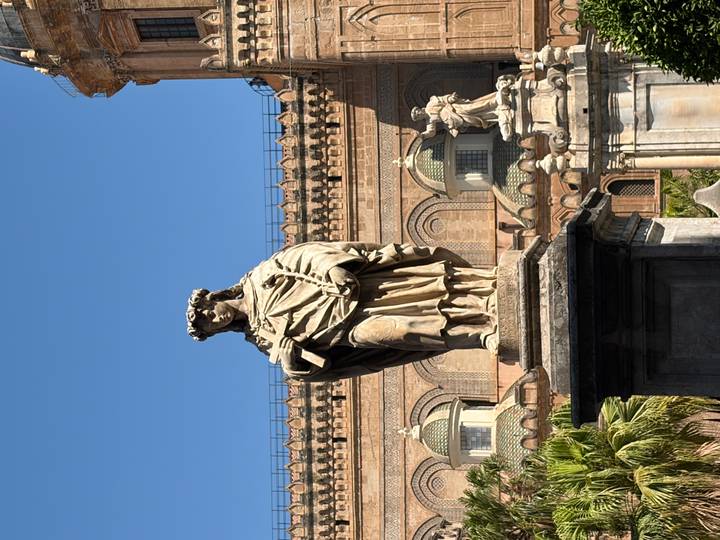 Stone statue in front of the ornate facade of Palermo Cathedral