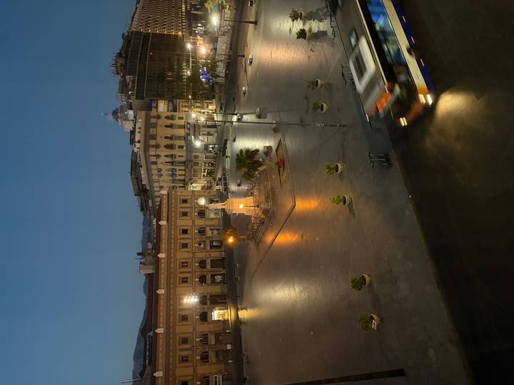 Early evening scene of Palermo city square with passing bus and lit buildings