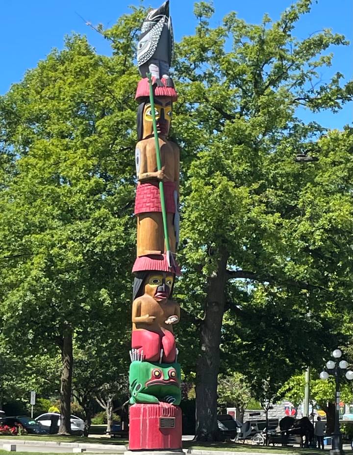 Totem pole featuring carved indigenous figures set before leafy green trees