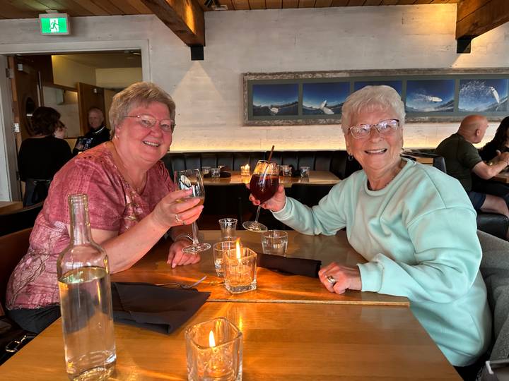 Two women toast with drinks inside a cozy restaurant with candlelit table