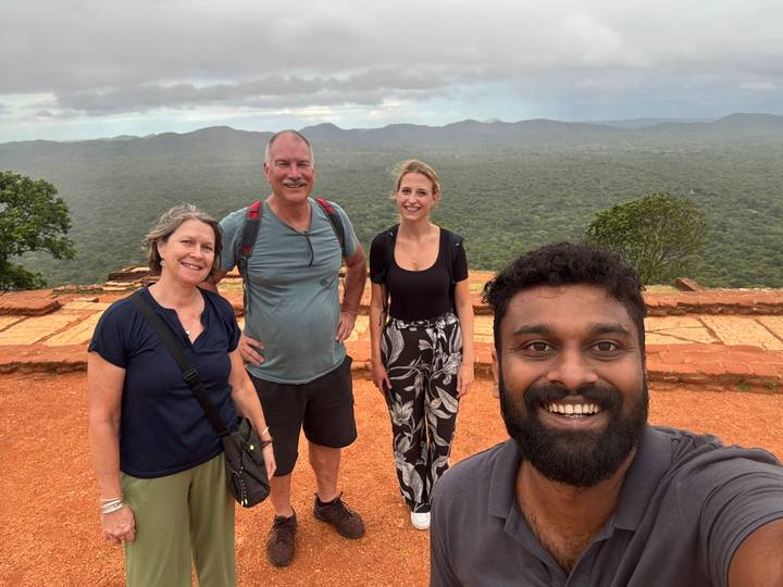 Four smiling travellers pose for a selfie on a rocky viewpoint overlooking dense forest
