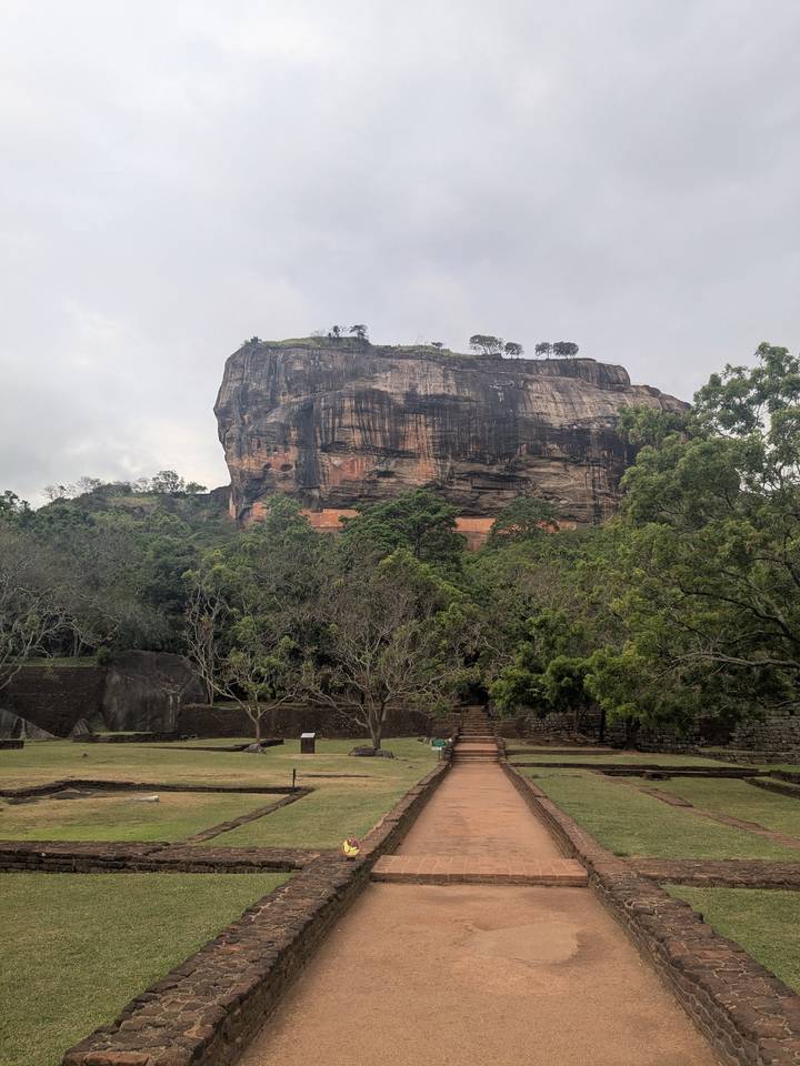 Massive Sigiriya Rock fortress rises above dense green forest on an overcast day