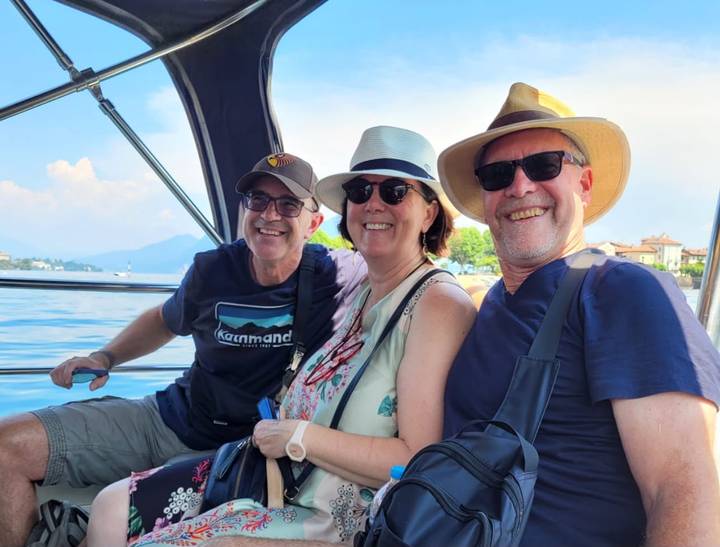 Three cheerful travellers in hats enjoying a boat ride on a sunny lake.