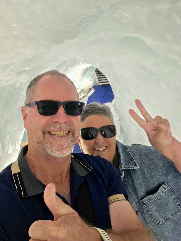 Smiling couple wearing sunglasses inside an icy tunnel flashing a peace sign.
