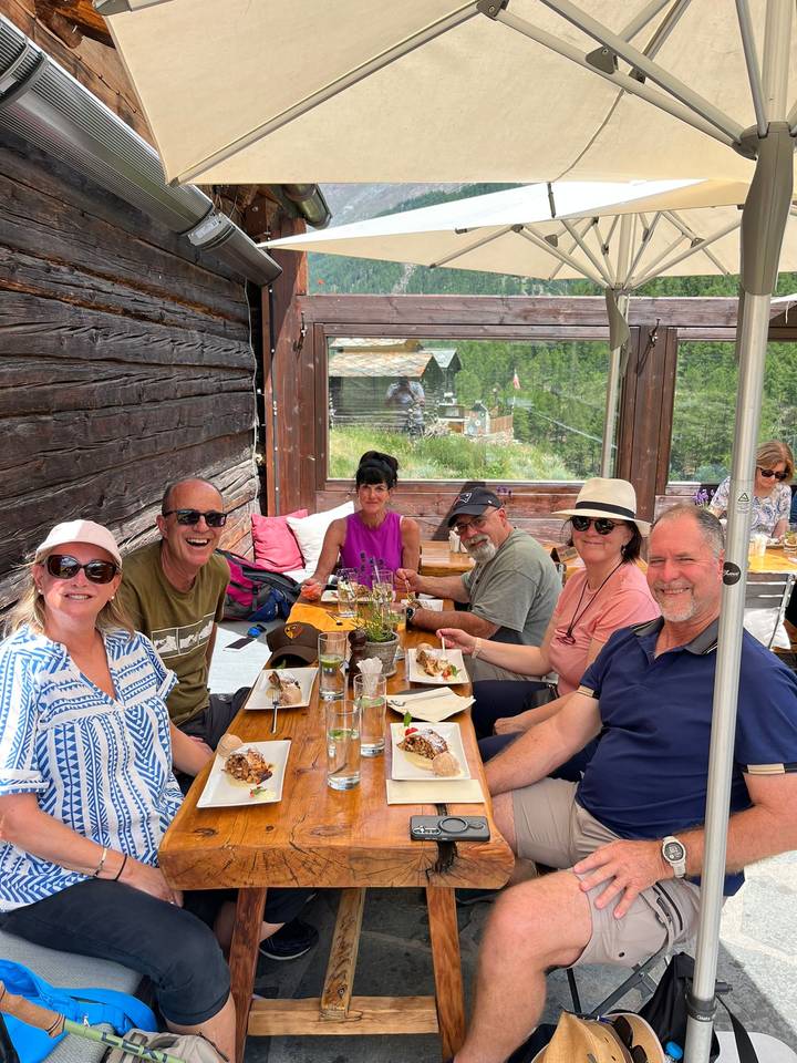 Small group enjoying lunch on a rustic wooden terrace overlooking alpine scenery.