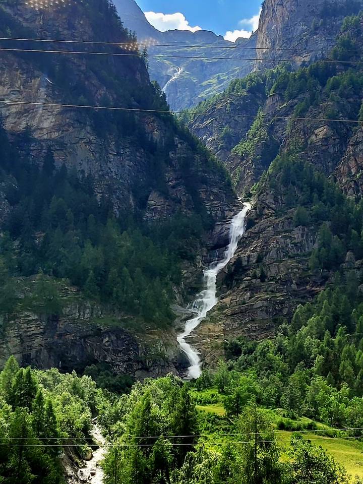 Tall waterfall cascading through a forested alpine gorge.