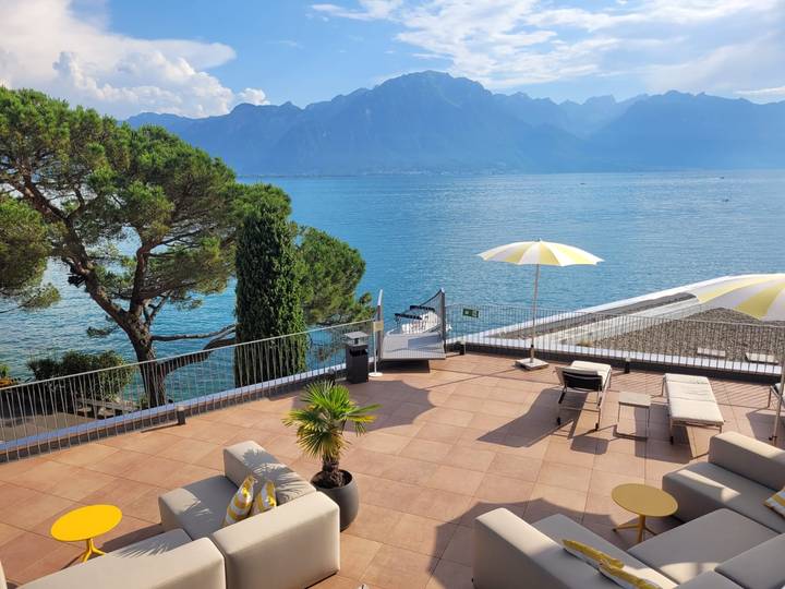 Terrace with loungers and yellow umbrellas overlooking a tranquil blue lake and mountains.