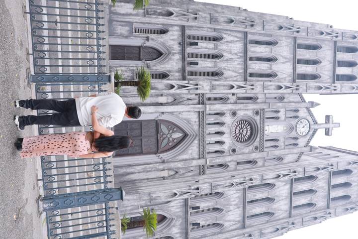 Couple standing arm-in-arm facing the gothic façade of St. Joseph’s Cathedral in Hanoi.