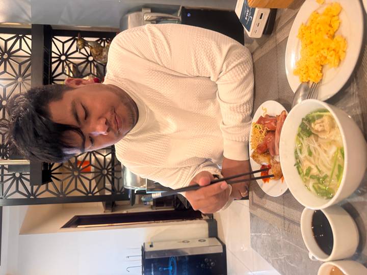 Man eats breakfast with chopsticks at a restaurant table set with soup and eggs.