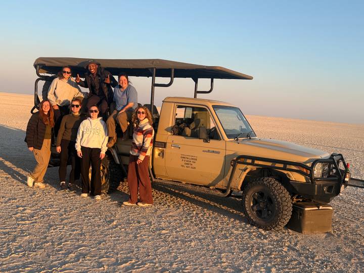 Tourists stand by an open safari vehicle on the vast white expanse of the Makgadikgadi salt pans at golden hour.
