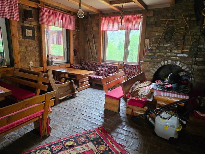 Cozy mountain hut interior with wooden benches, checkered textiles and a stone fireplace.