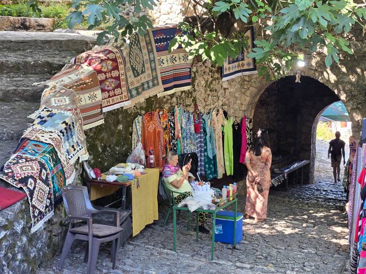Market stall under stone arch selling colourful textiles and dresses in a Bosnian old town.
