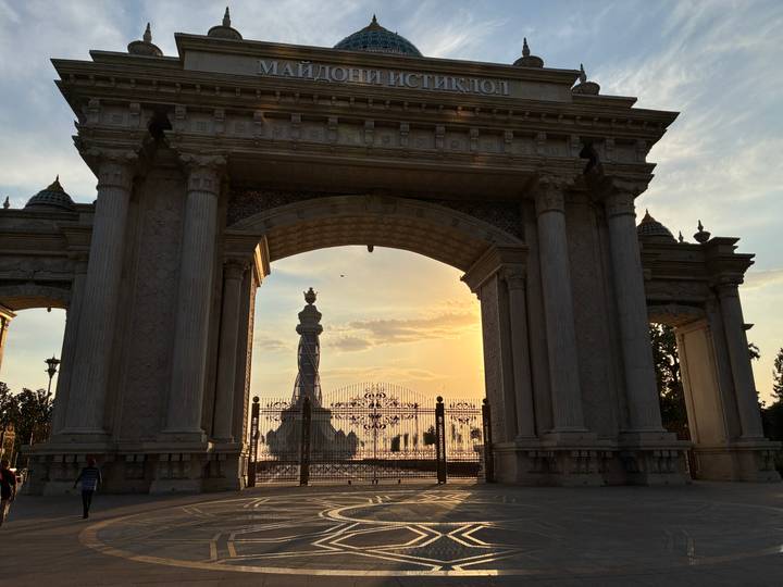 Grand neoclassical archway framing a monument at golden sunset in a Central Asian capital.