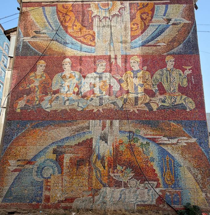 Colorful Soviet-era mosaic mural depicting figures with goblets and industrial themes.