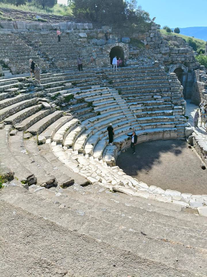 Stone seating tiers of an ancient amphitheatre with two visitors standing on the stage.