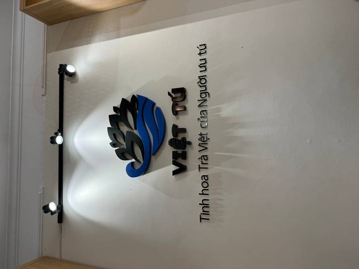 Wall logo and Vietnamese text for 'Việt Tú' tea brand under spotlights.