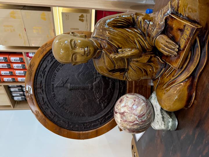 Ceramic monk statue displayed with stone sphere and carved wooden disk in shop.