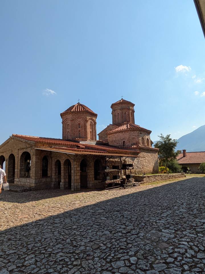 Historic Byzantine church complex with brick domes and stone courtyard in sunlight.