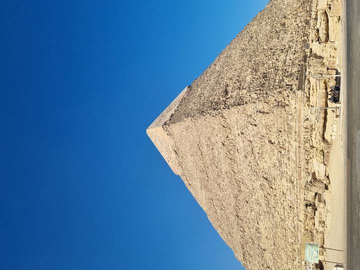 A single limestone pyramid stands sharply against a vivid blue sky.